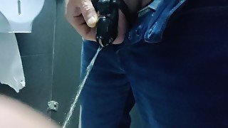 Locked in a chastity cage, man is pissing in a public toilet
