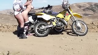Daring doll in motocross boots is bent over a dirt bike and screwed in the desert.