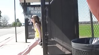 Young beauty in a pretty yellow top is recorded while she waits for the bus in the sun.