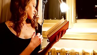 Incredibly sexy redhead enjoys reading a book by lamplight next to her window