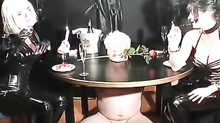 Brunette mistress in latex suit torturing her slave with his head inide table with rose thorns